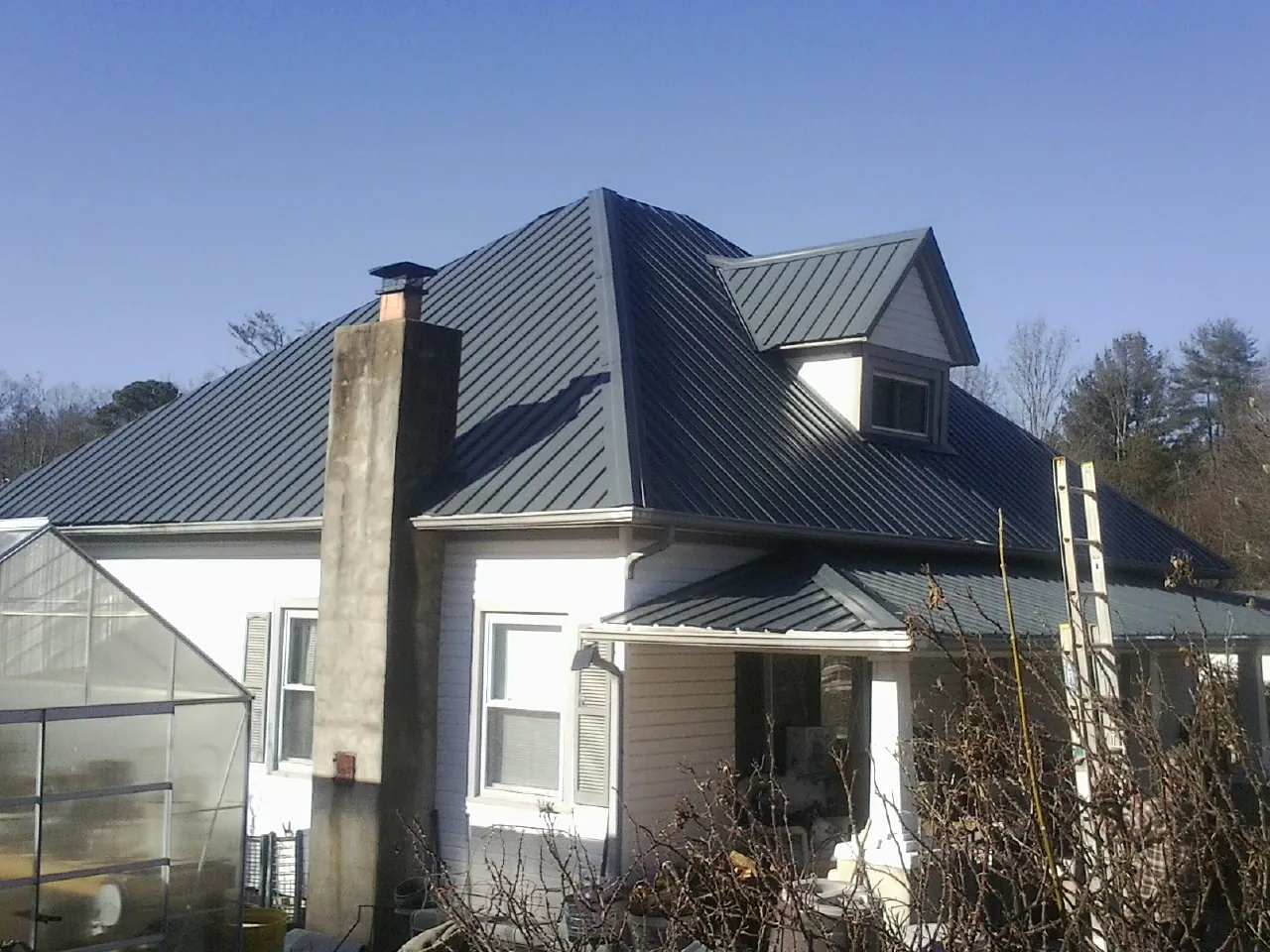 Dark blue standing seam metal roof on a white farmhouse with dormer — Slate & Tile Roof Repair by Roofing Brothers in King