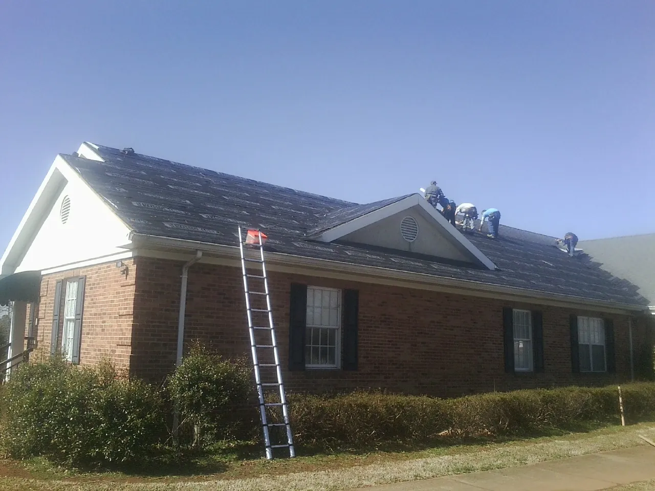 Crew tearing shingles off a brick ranch roof with a ladder set — Emergency Roof Repair work by our crew in King