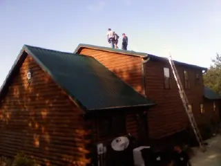 Crew on the ridge of a green metal roof on a two story log home in King